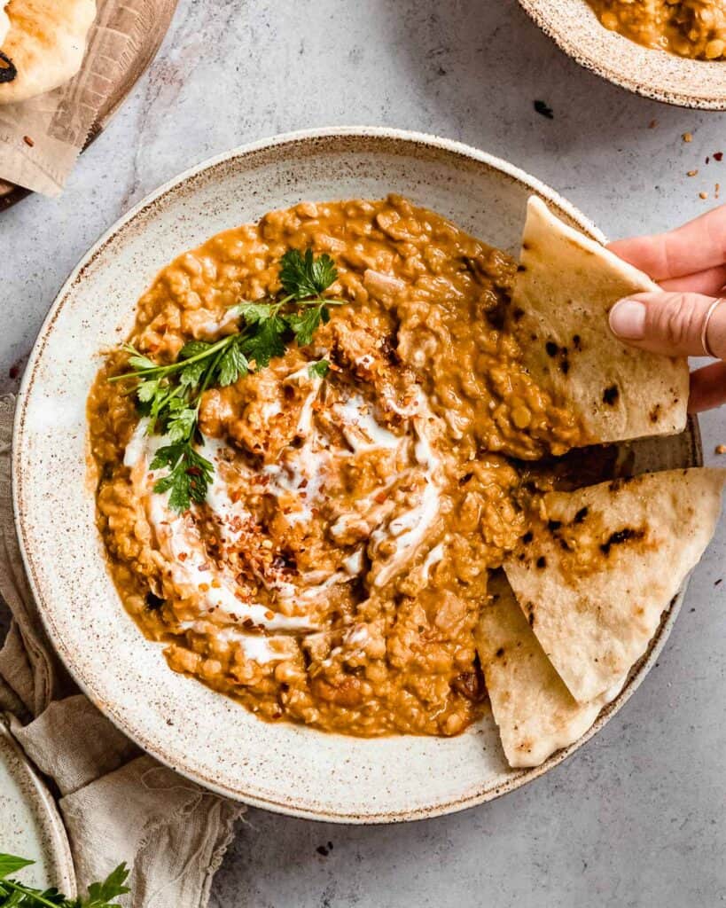 big bowl of coconut red lentil dahl in a bowl, next to it some naan bread.