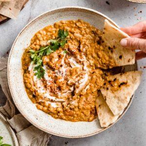 big bowl of coconut red lentil dahl in a bowl, next to it some naan bread.