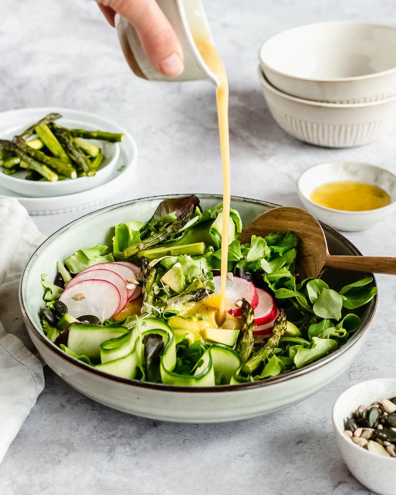 asparagus green salad with dressing being poured on top.