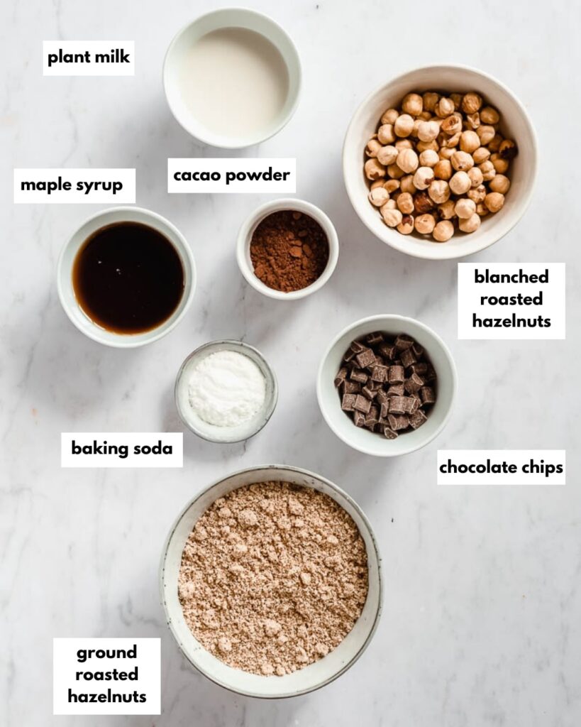 all ingredients needed for chocolate hazelnut brownies: maple syrup. cocao powder, blanched roasted hazelnuts, chocolate chips, baking soda, ground roasted hazelnuts, plant milk
