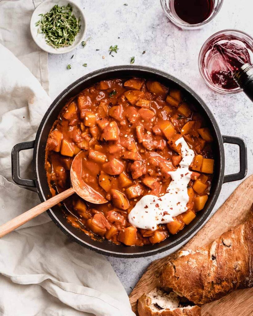 big pot of potato goulash with some red wine on the side
