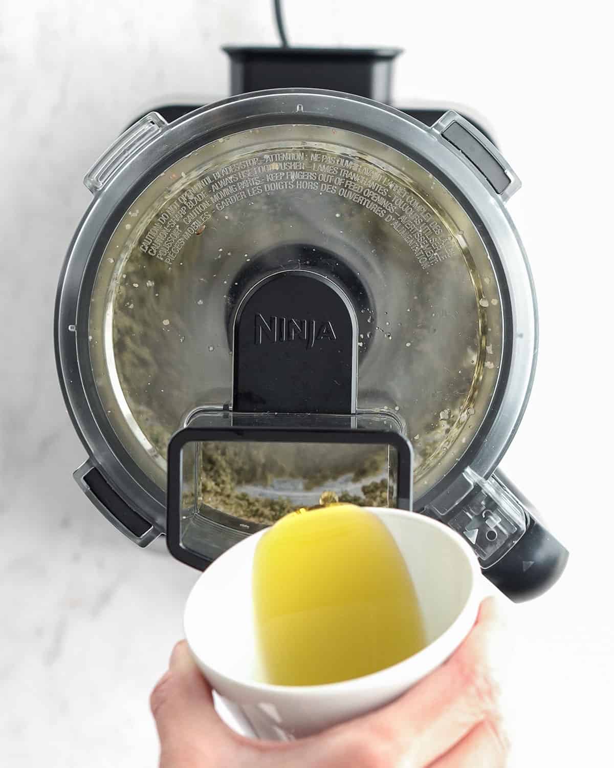 olive oil being poured into food proseccor while blending.