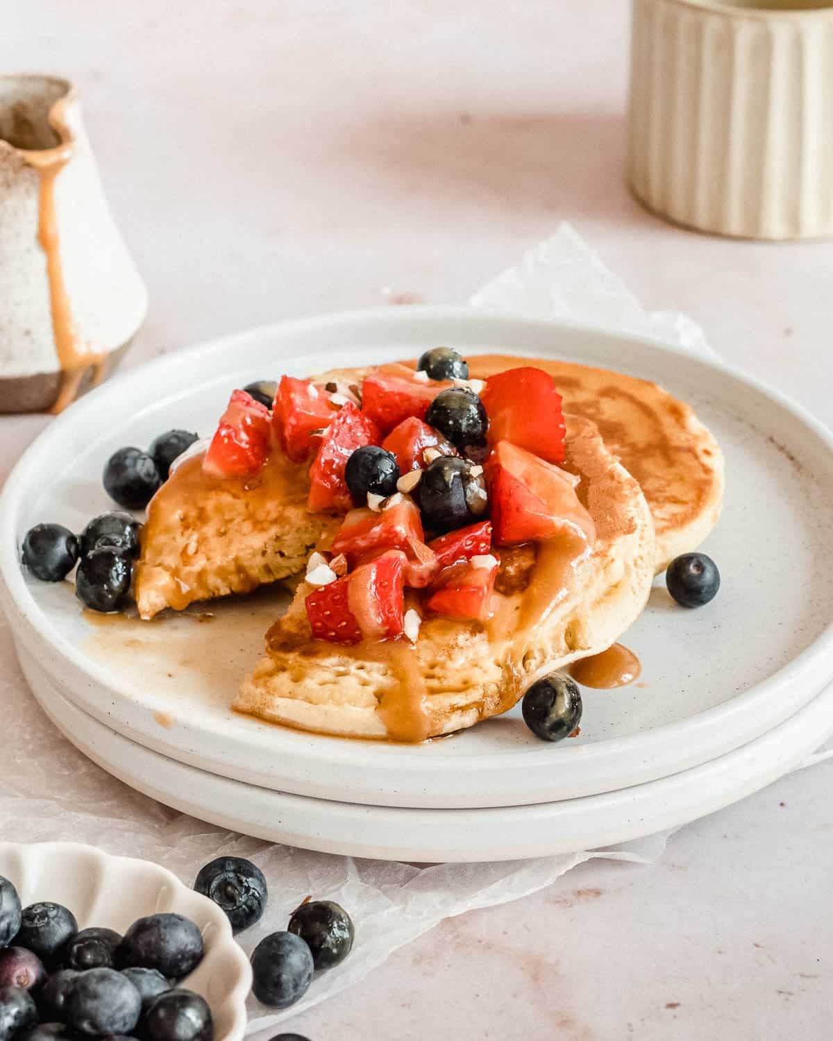 2 oatmilk pancakes on a plate topped with vegan caramel sauce and fresh berries.