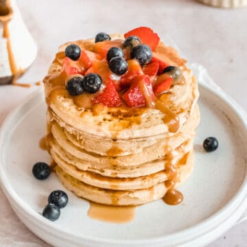 stack of oatmilk pancakes topped with fresh strawberries and blueberries.