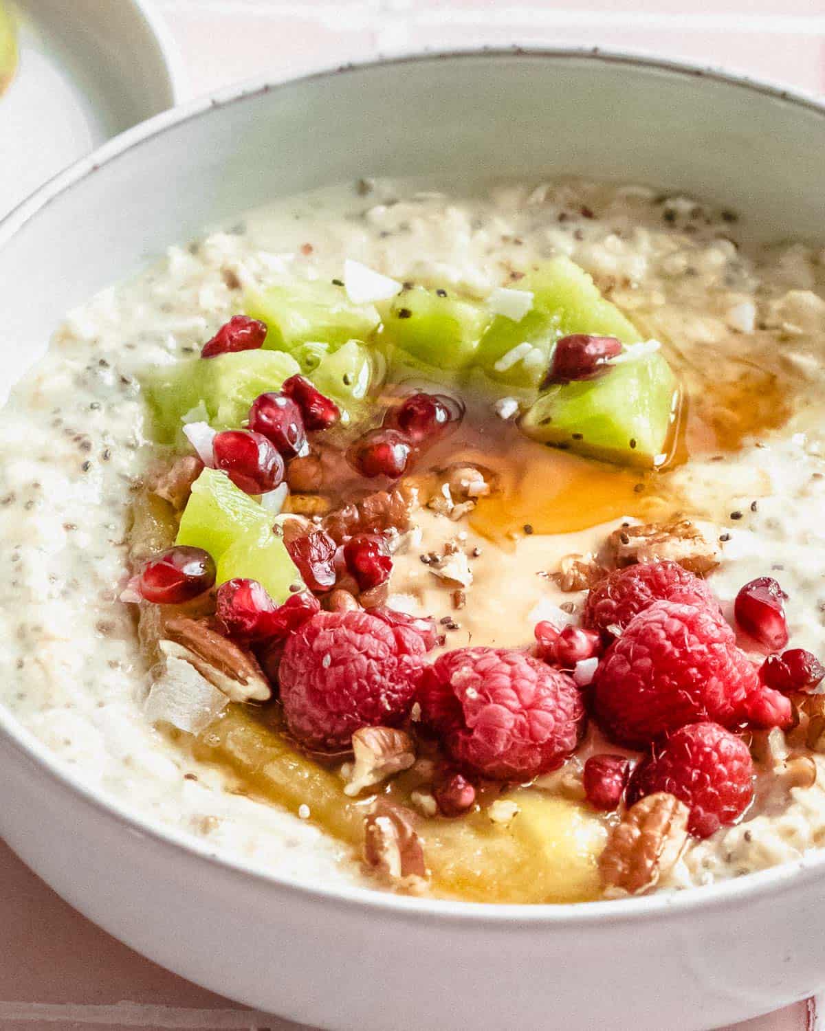 overnight oats in a bowl topped with fresh raspberries and kiwi with a generous drizzle of maple syrup.