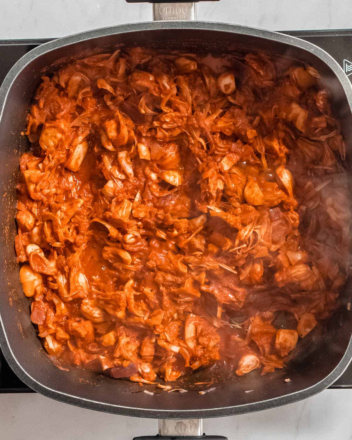 finished birria jackfruit sauce with jackfruits simmering in a large frying pan.