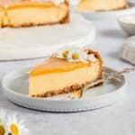 1 slice of mango cheesecake on a plate with a fork next to it.