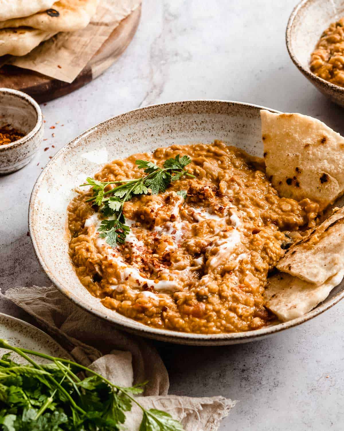 big bowl of red lentil dahl with some naan bread and topped with fresh herbs and yogurt.