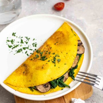 Omelette stuffed with spinach and mushrooms on a plate topped with chopped parsley with a fork beside.