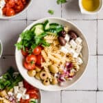 big bowl of greek pasta salad with dressing on the side.