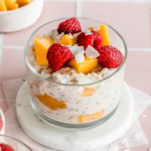 small jar of overnight oats with coconut milk topped with fresh raspberries and mango pieces.