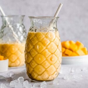 2 glasses of mango smoothie without yogurt, next to tit some fresh mango.
