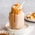 banana milkshake in a serving glass topped with whipped cream and caramel sauce drizzled on top.