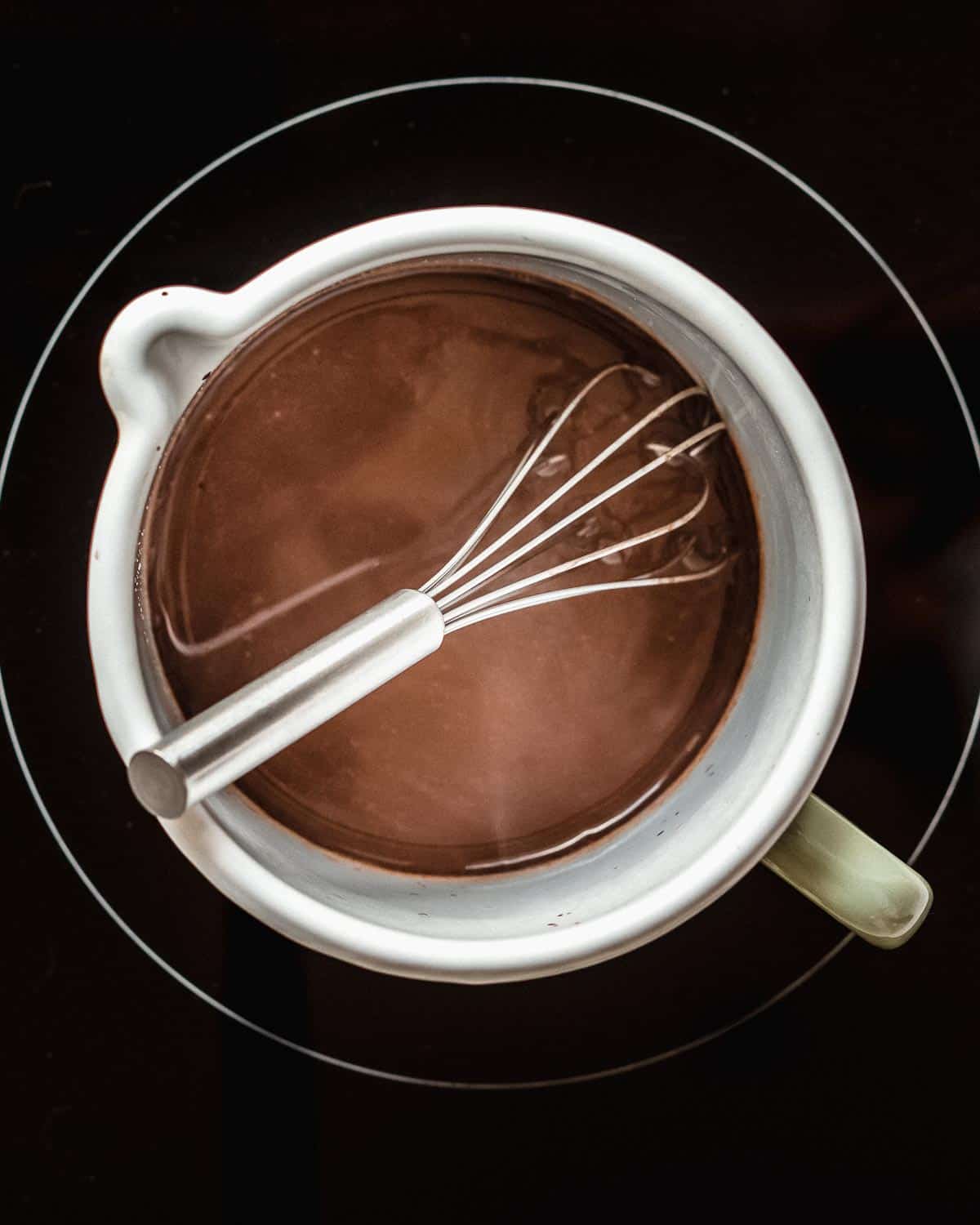 milk cocoa powder and sugar added to a saucepan with a whisk in it.