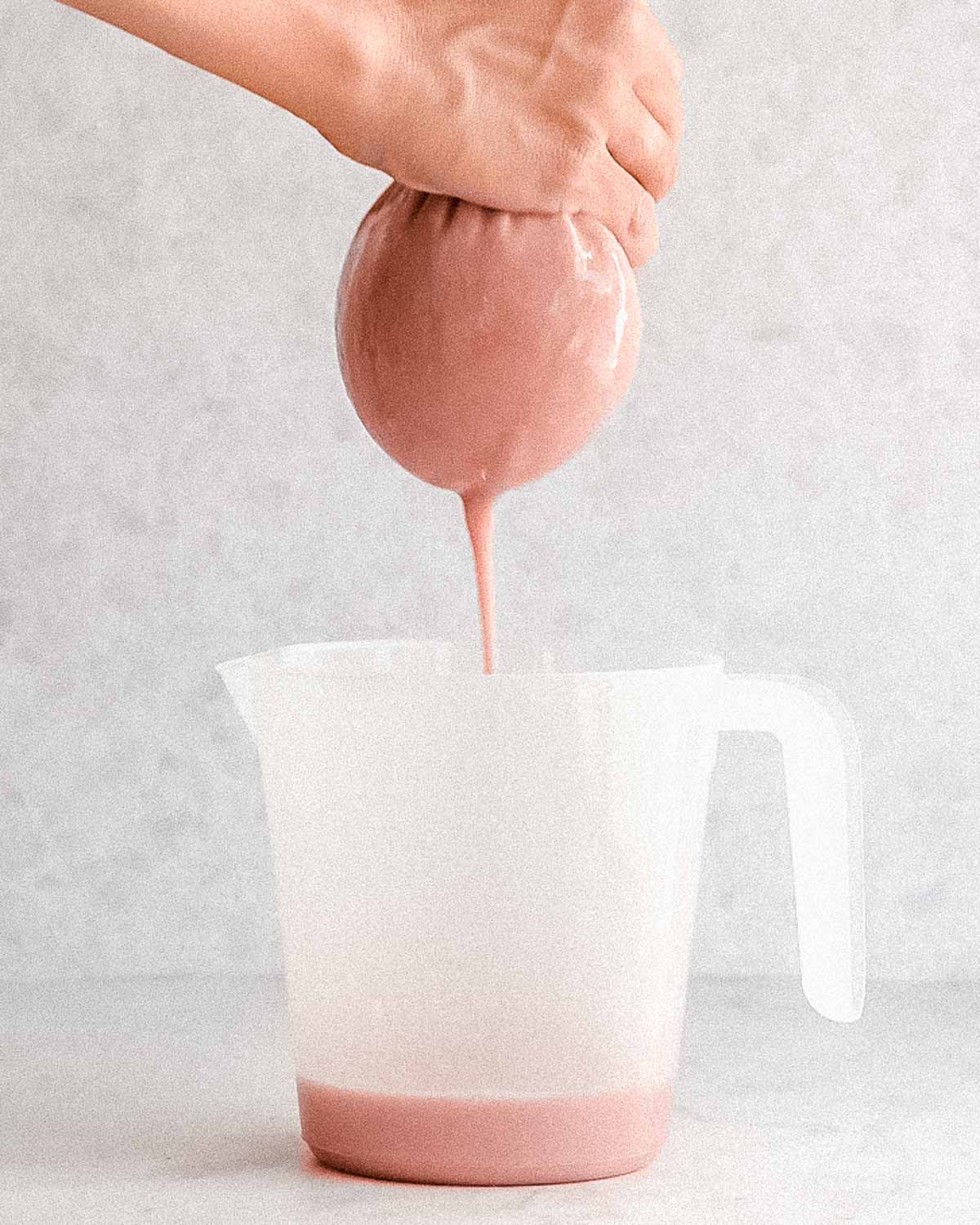 strawberry milk being squeezed from a nut milk bag into a measuring cup.