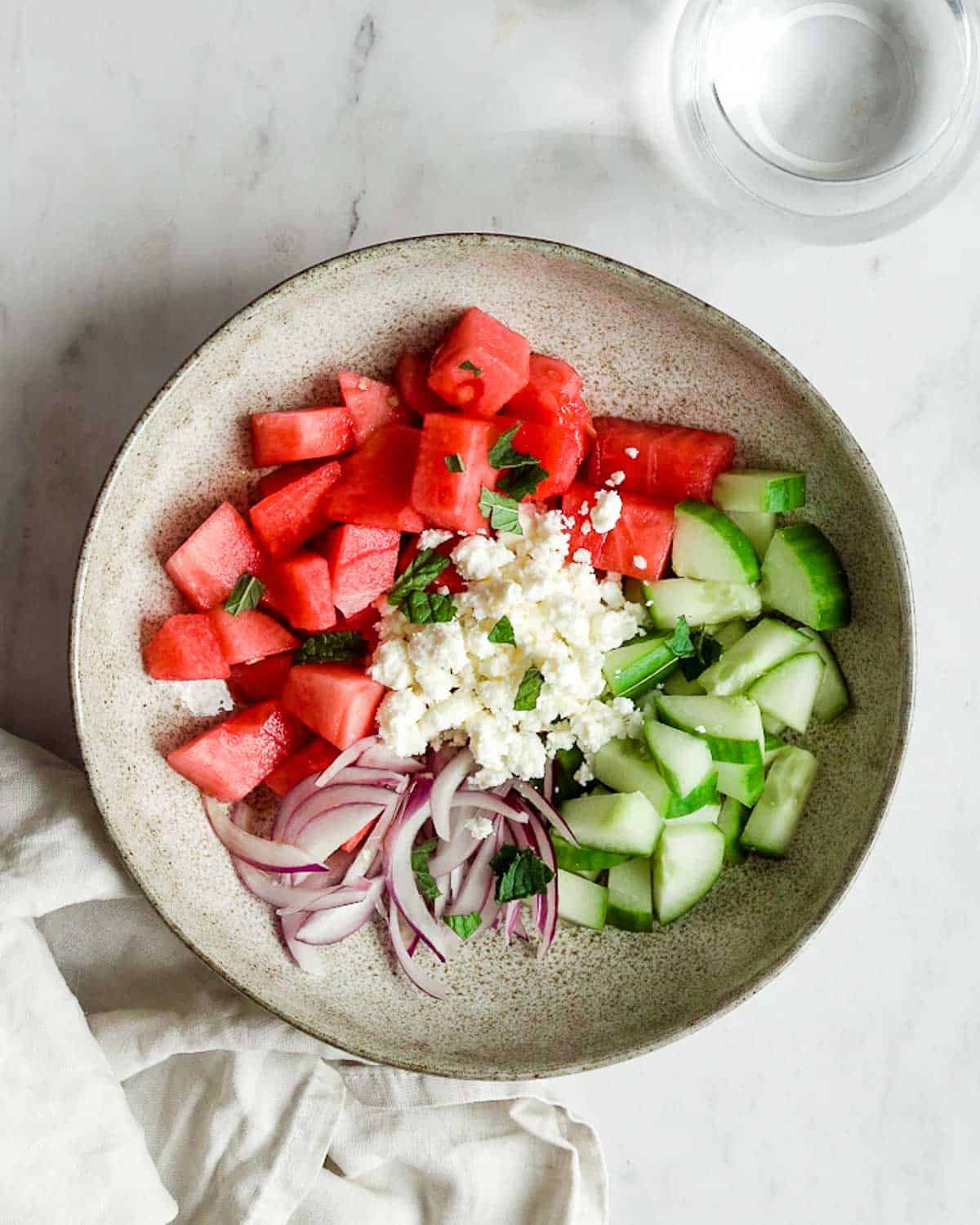 watermelon, feta, cucumber, red onion and mint leaves in a bowl.