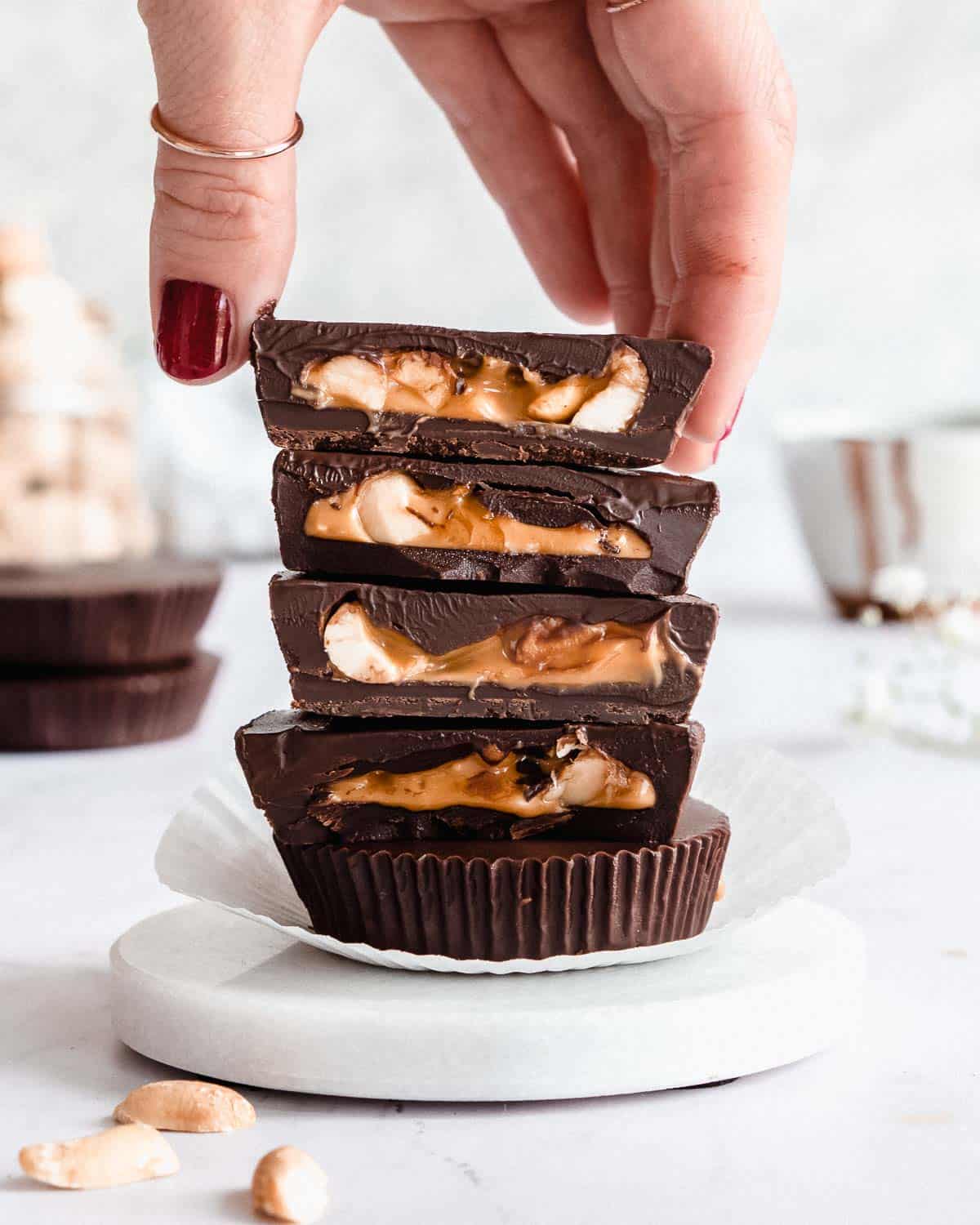 stack of 5 peanut butter cups on a marble plate, one hand lifting off the first cup.
