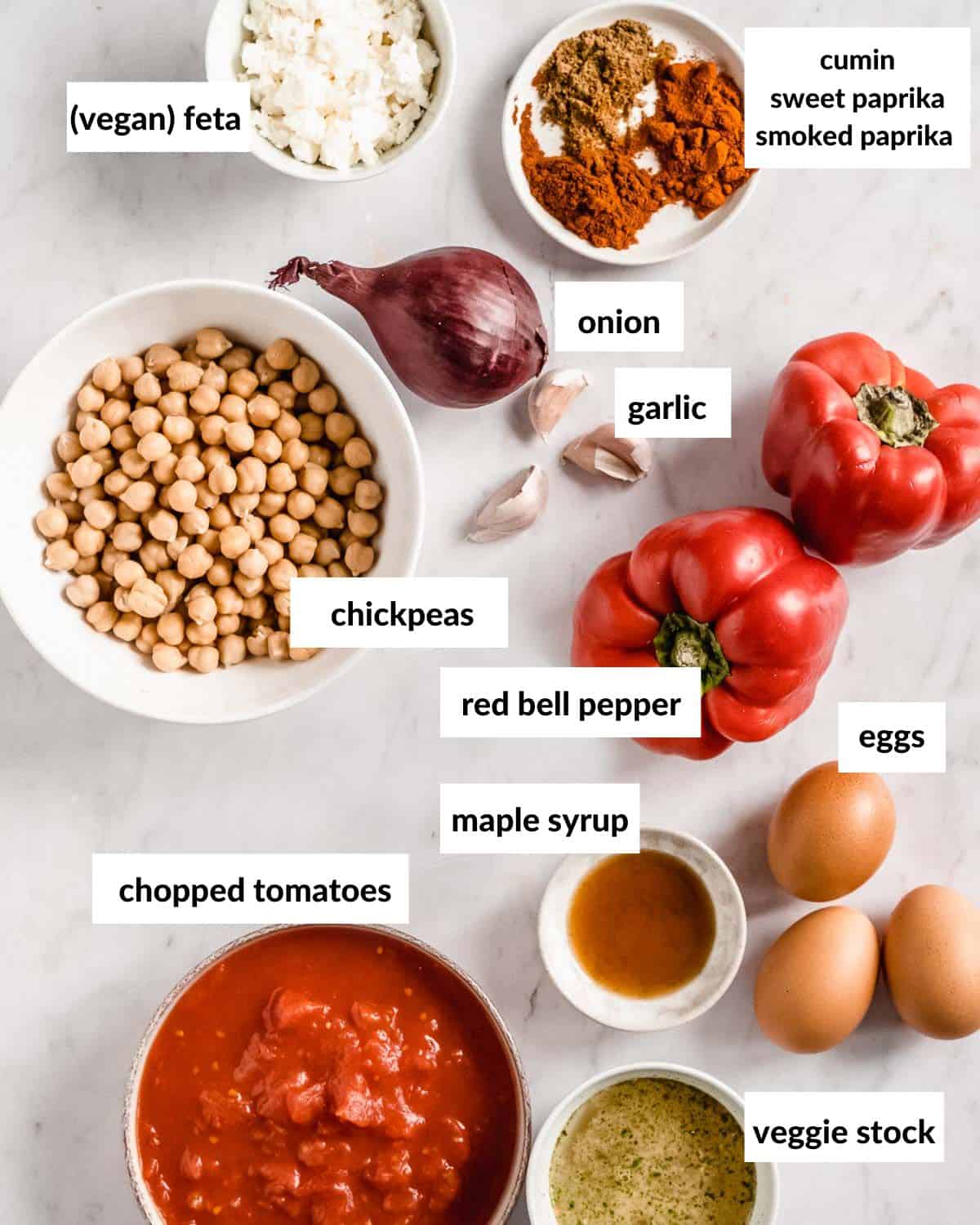 all ingredients needed to make vegetarian shakshuka: onion, garlic cumin, sweet paprika, smoked paprika, red bell pepper, eggs, maple syrup, chopped tomatoes, veggie stock, chickpeas, vegan feta.