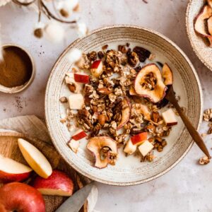 big bowl with milk and cinnamon maple granola, apple pieces and sliced apples next to it.