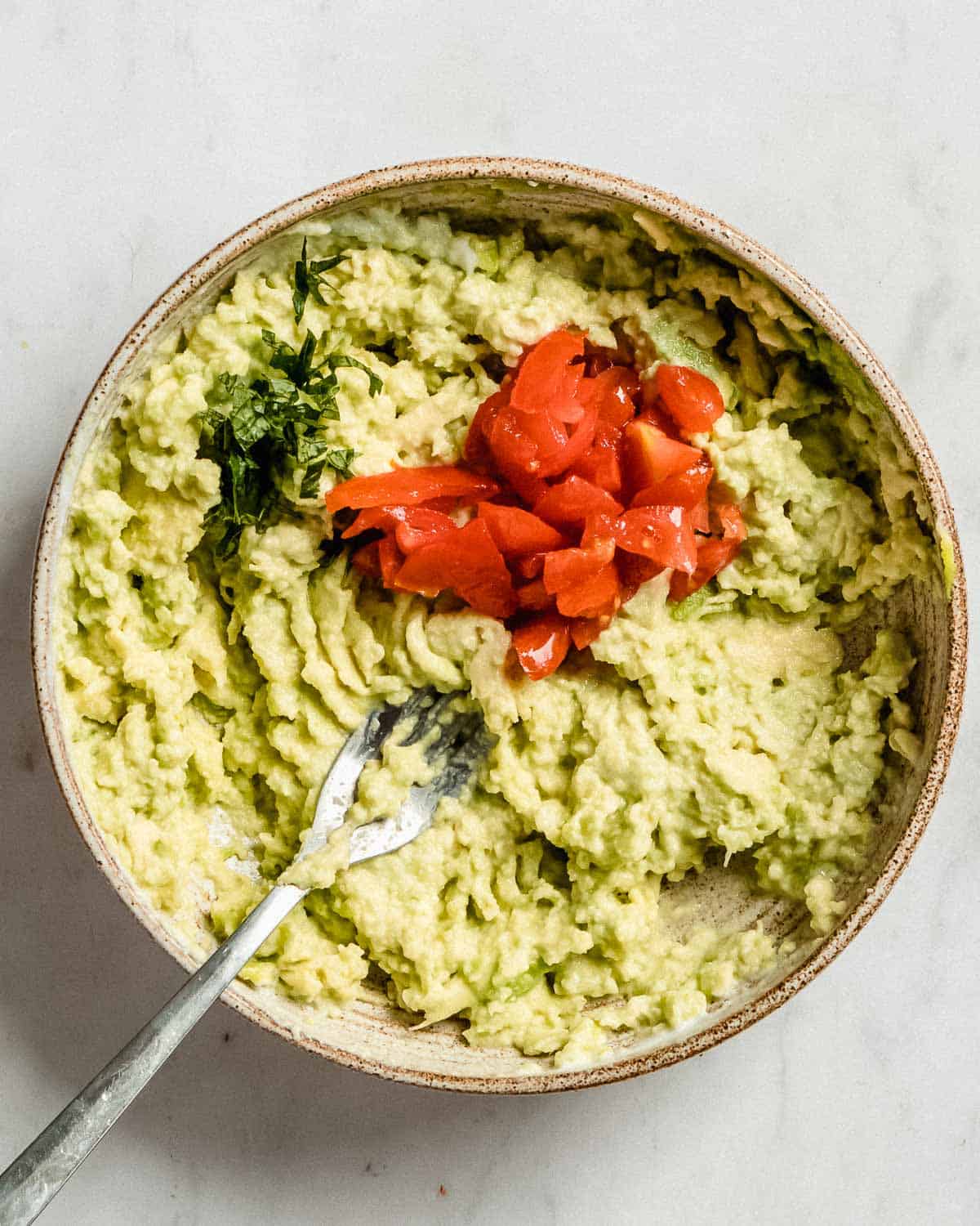 guacamole in a bowl with added cilantro and cherry tomatoes.