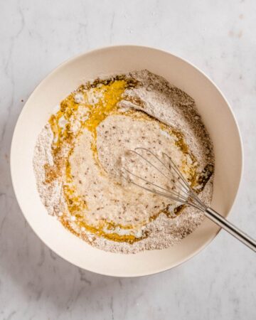 dry ingredients and wet ingredients in a mixing bowl with a whisk in it.