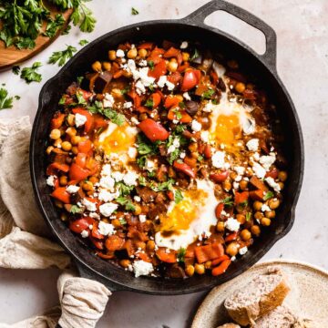 shakshuka in a big cast iron pan with three eggs, next to it some bread and fresh parsley.
