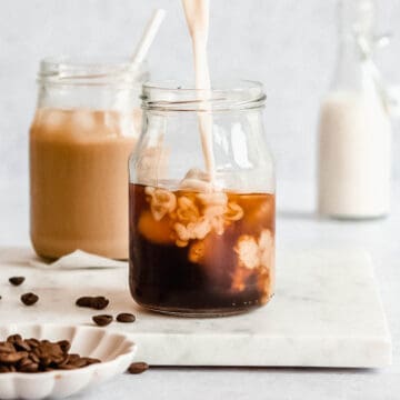 serving glass filled with ice and french press cold brew and milk being poured on top.