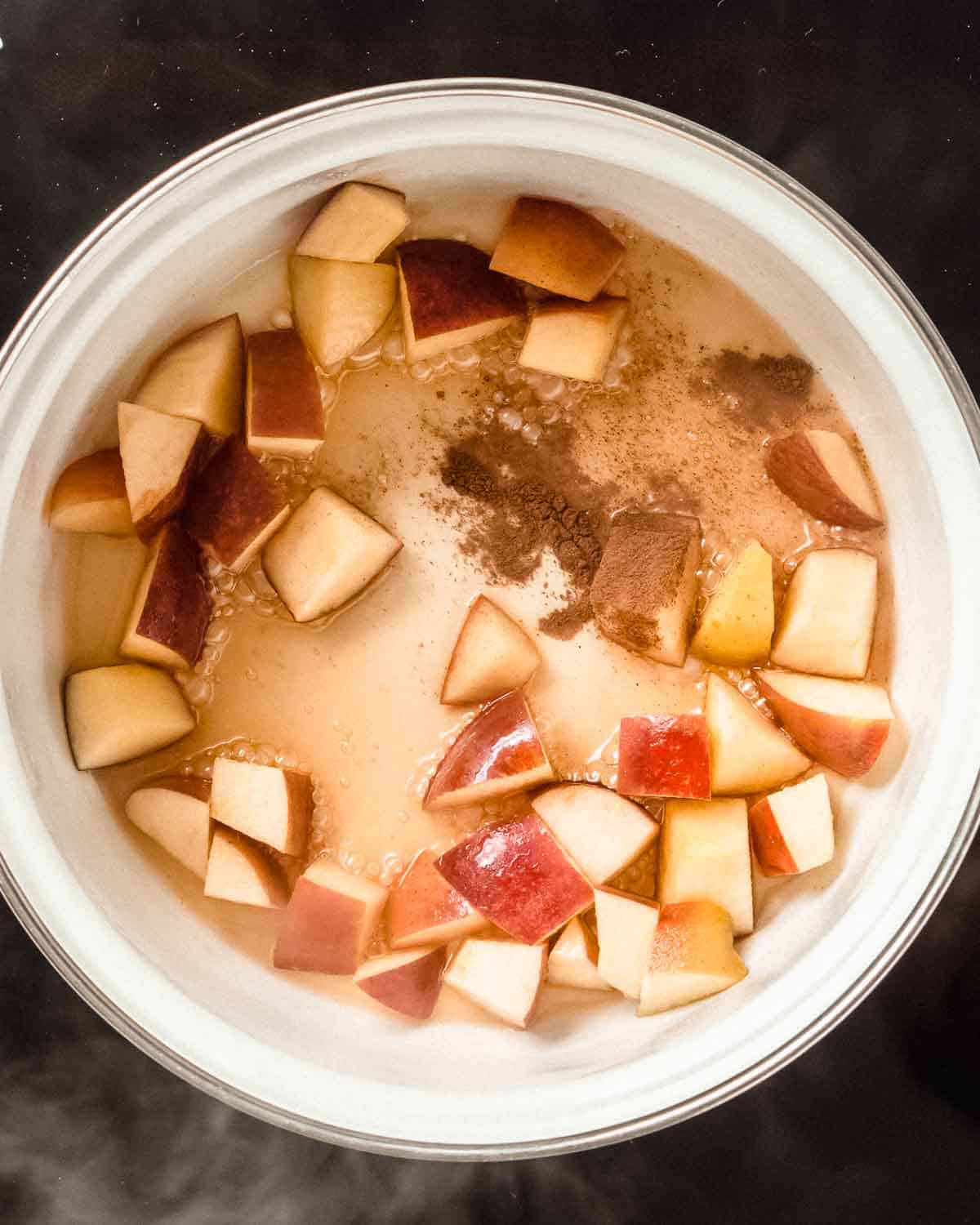 diced apples, cinnamon, maple syrup and water simmering in a saucepan.