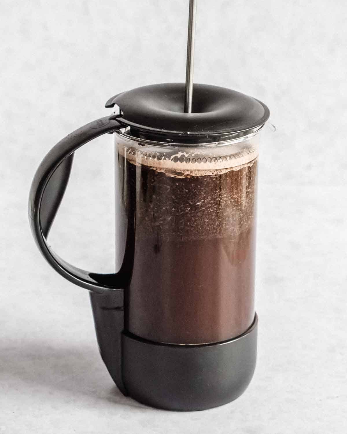french press filled with water and ground coffee and a lid added.