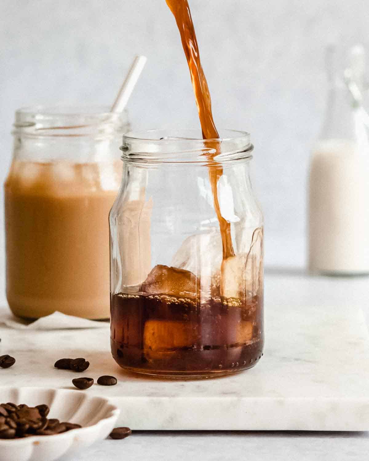 cold brew coffee being added to a serving glass filled with ice.