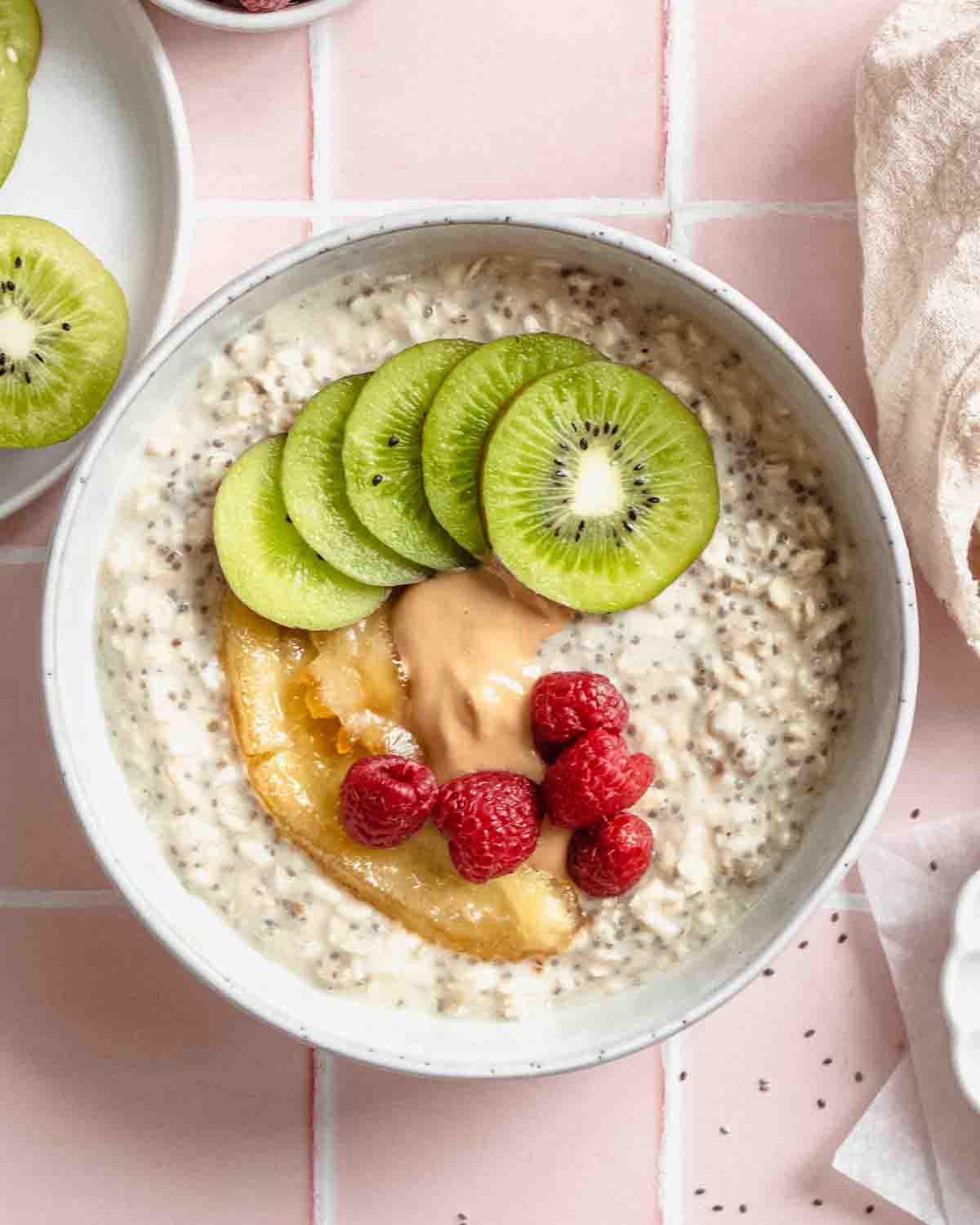 overnight oats in a bowl topped with kiwi, raspberries, caramelized banana and peanut butter.