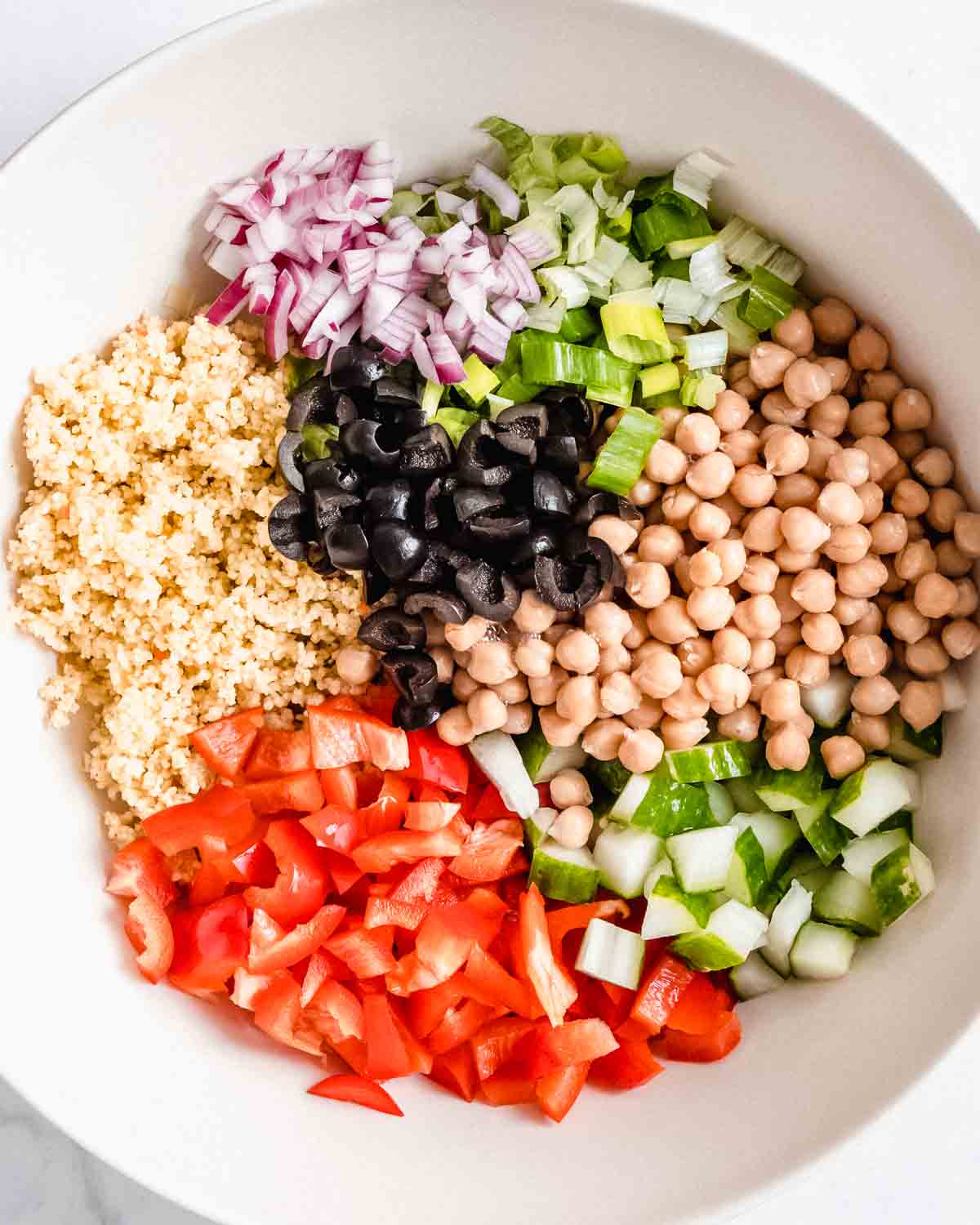 cooked couscous, red bell pepper, cucumber, chickpeas, green onion, red onion and chopped black olives added to a large bowl.
