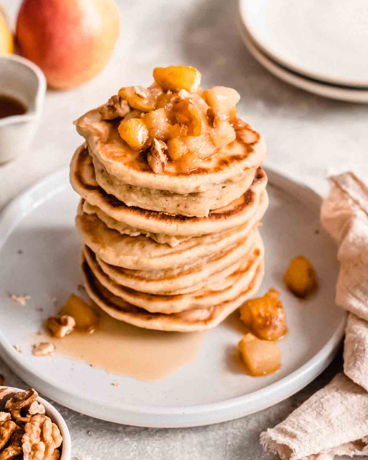 stack of 6 pear pancakes on a plate topped with caramelized pear and maple syrup.