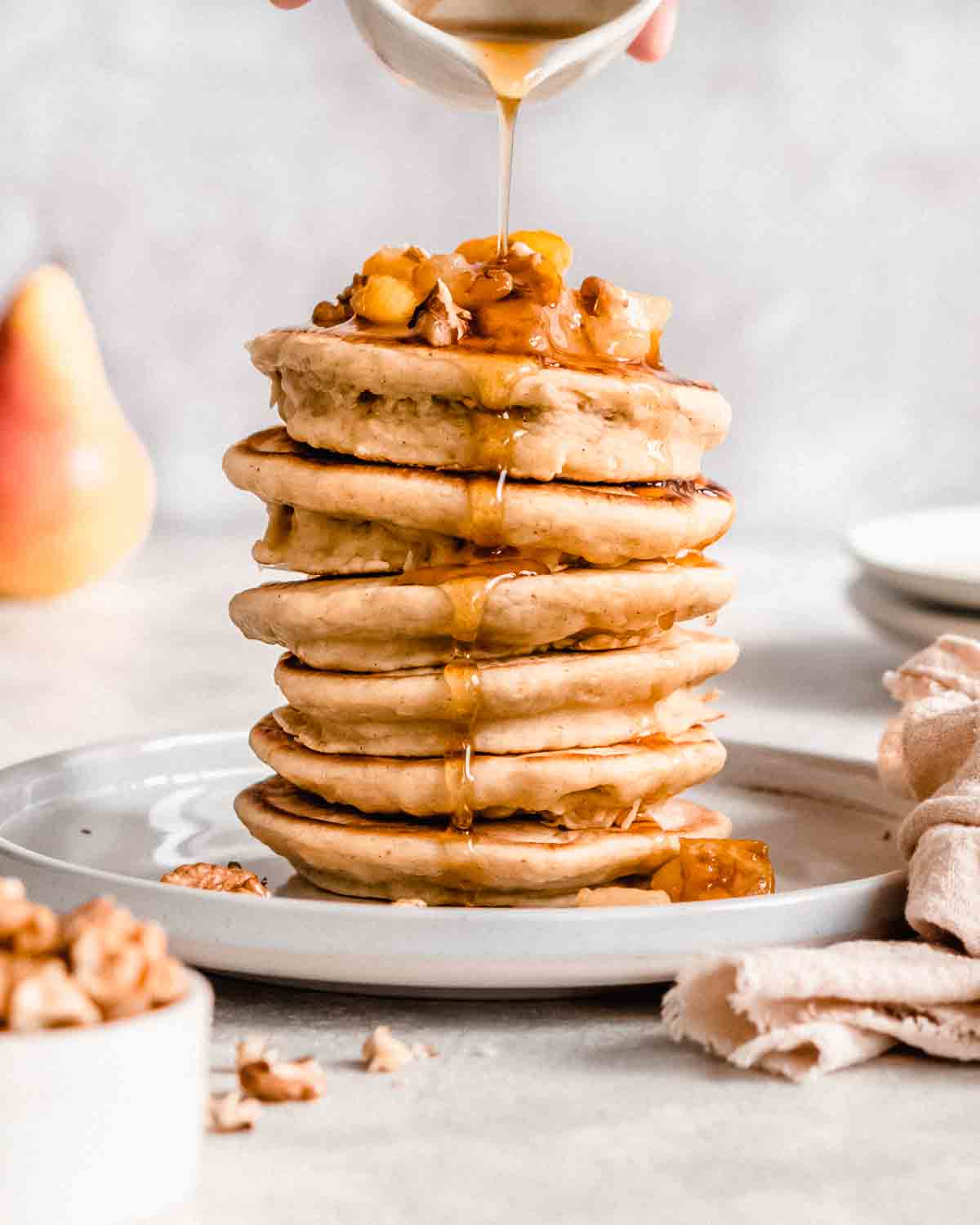stack of 6 pear pancakes topped with caramelized pear and maple syrup.