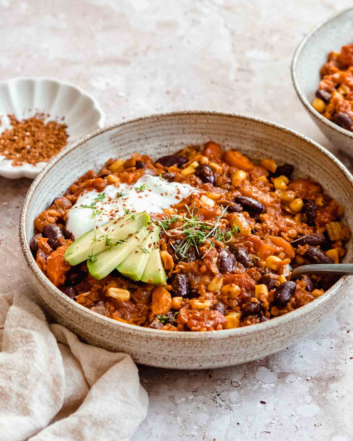 bowl of vegetarian chili con carne topped with fresh avocado slices and plain yogurt.