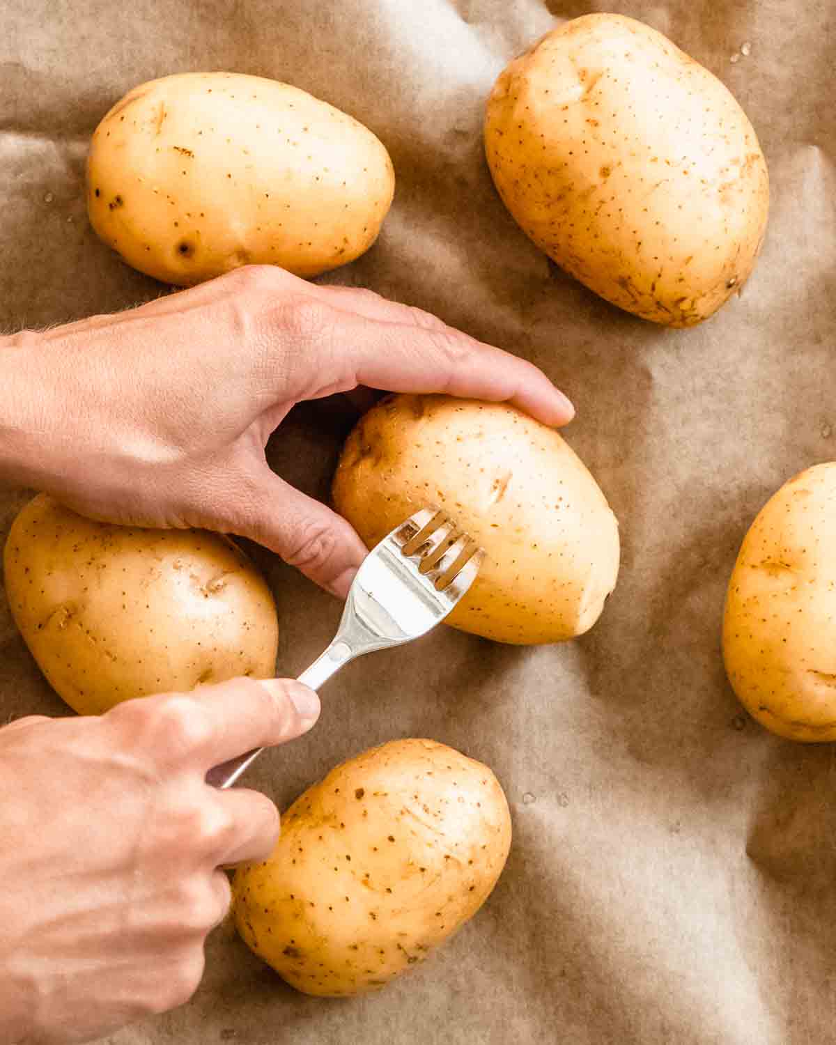 fork piercing holes into potatoes on a baking tray lined with parchment paper.