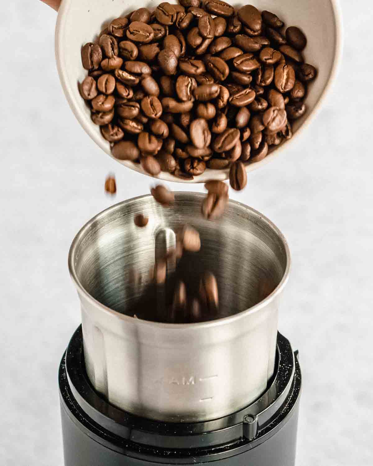 whole coffee beans being added to a coffee grinder.