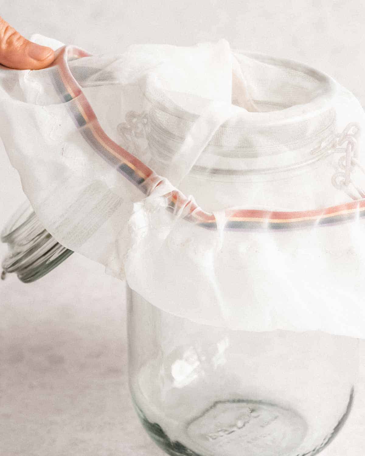 nut milk bag placed on a small fine-mesh sieve thats held above a wide-mouthed empty glass jar.