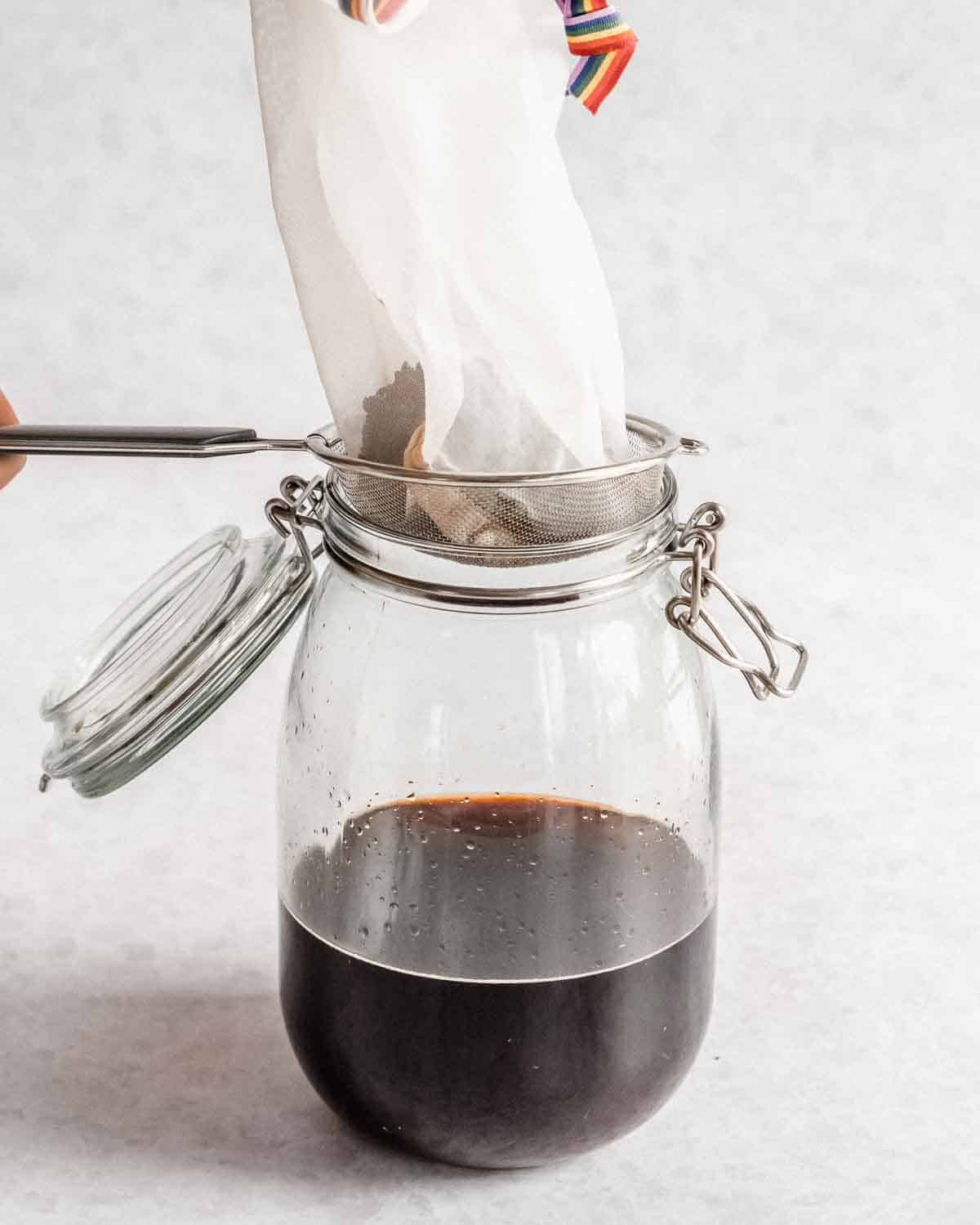 cold brew concentrate in a new glass jar, the coffee grounds being left behind in the sieve.