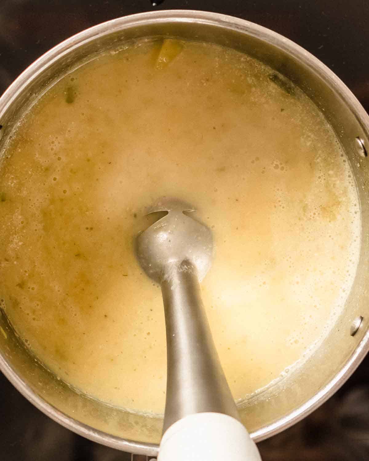 stick blender blending potato soup in a soup pot.