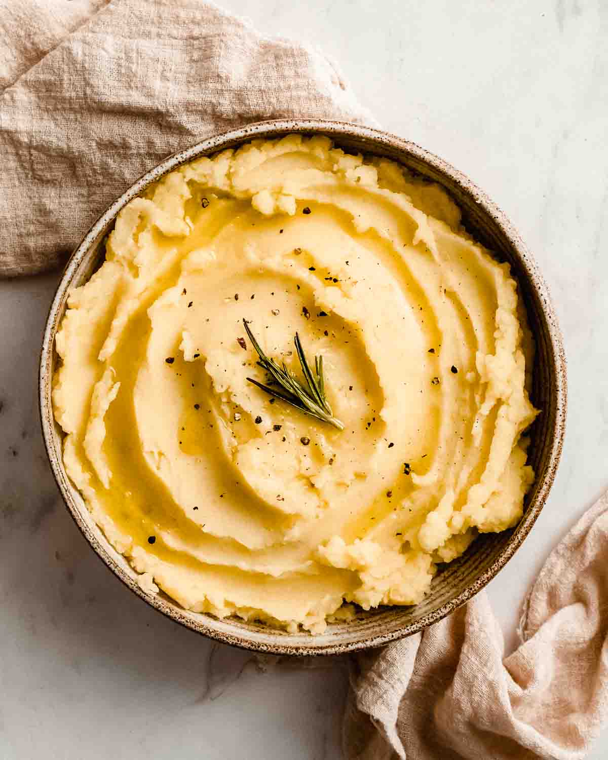 mashed potatoes without butter in a bowl topped with fresh rosemary and black pepper.