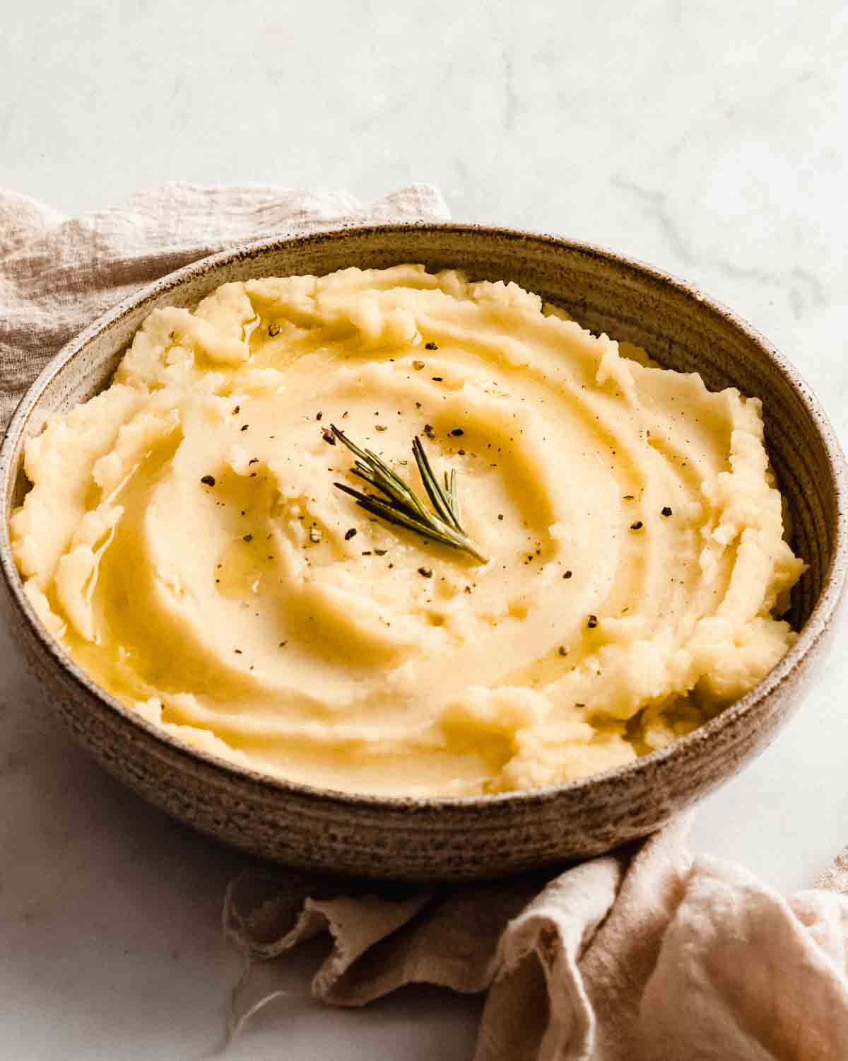 mashed potatoes in a bowl topped with fresh rosemary and black pepper.