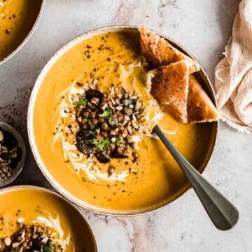 3 bowls of pumpkin carrot soup topped with roasted lentils, pumpkin seeds and fresh parsley and crusty bread.