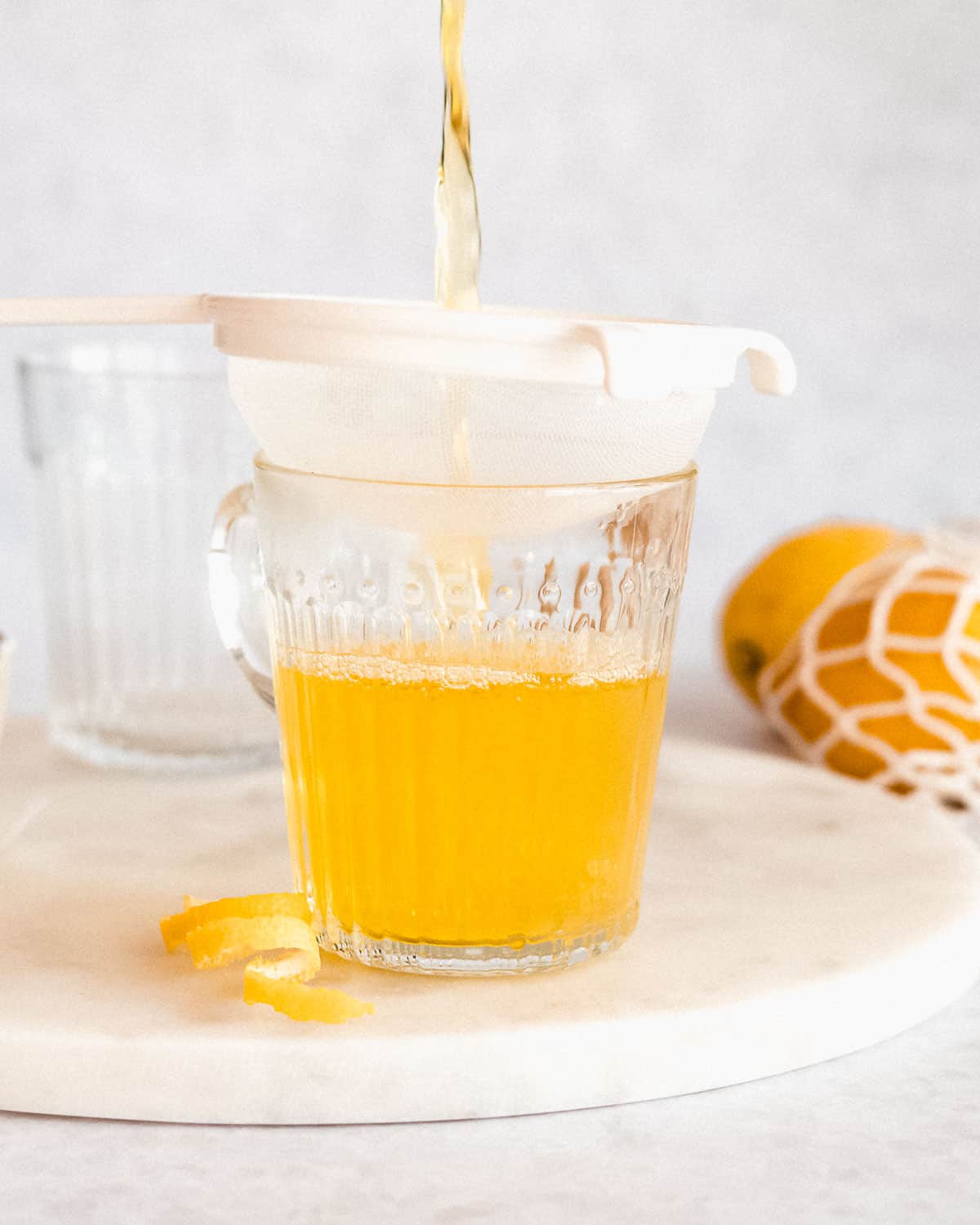 lemon ginger turmeric tea being poured through a fine mesh sieve into a cup.