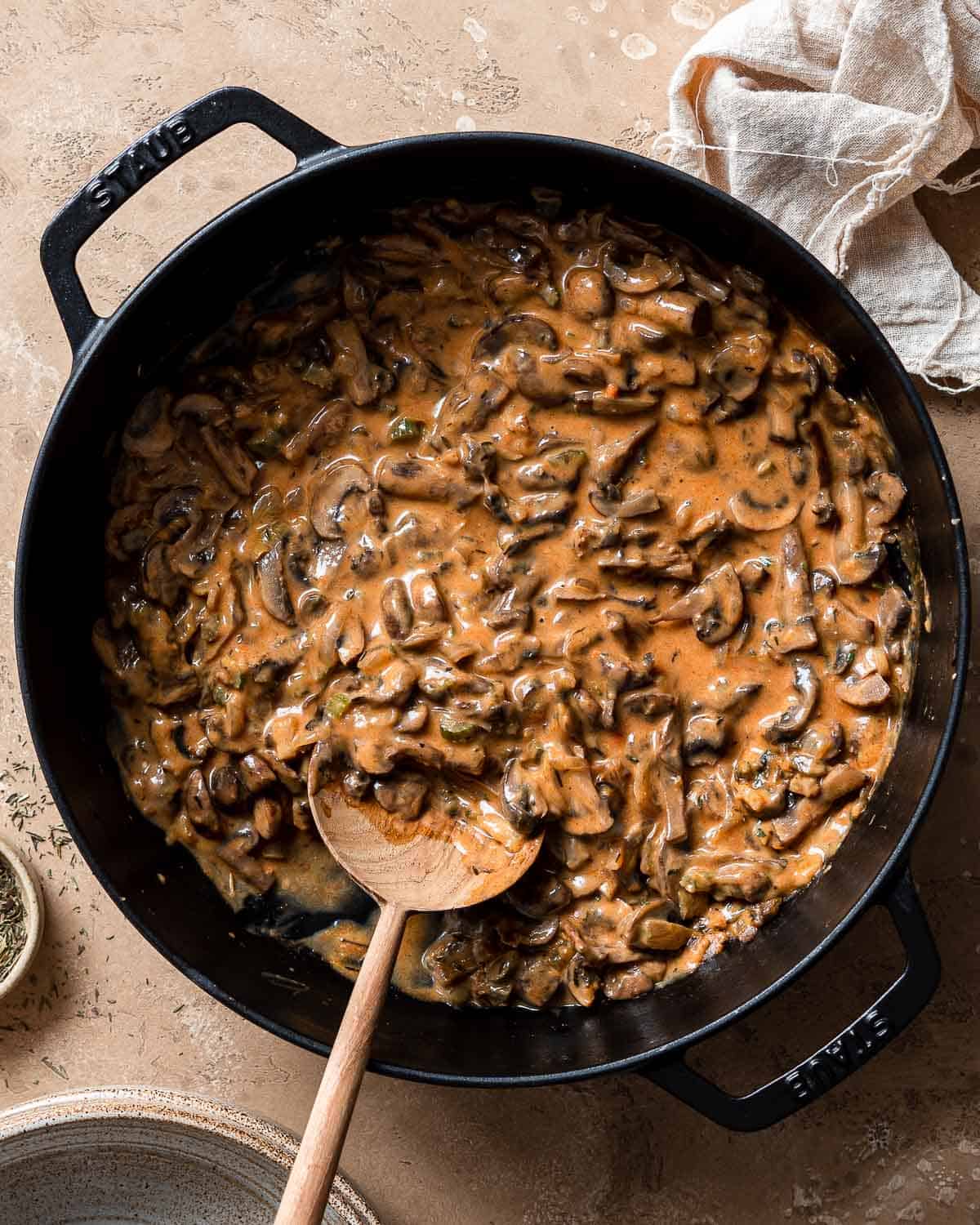 1 cast iron skillet filled with ragout of mushrooms and a wooden spoon.