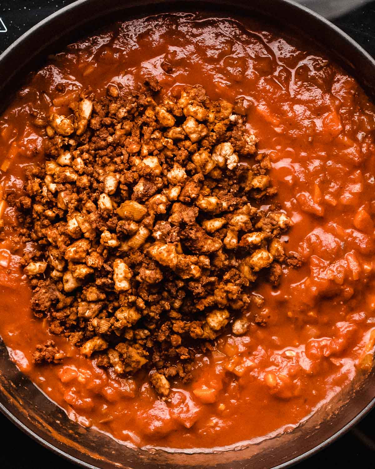 cooked tofu crumbles added to a tomato sauce in a saucepan.