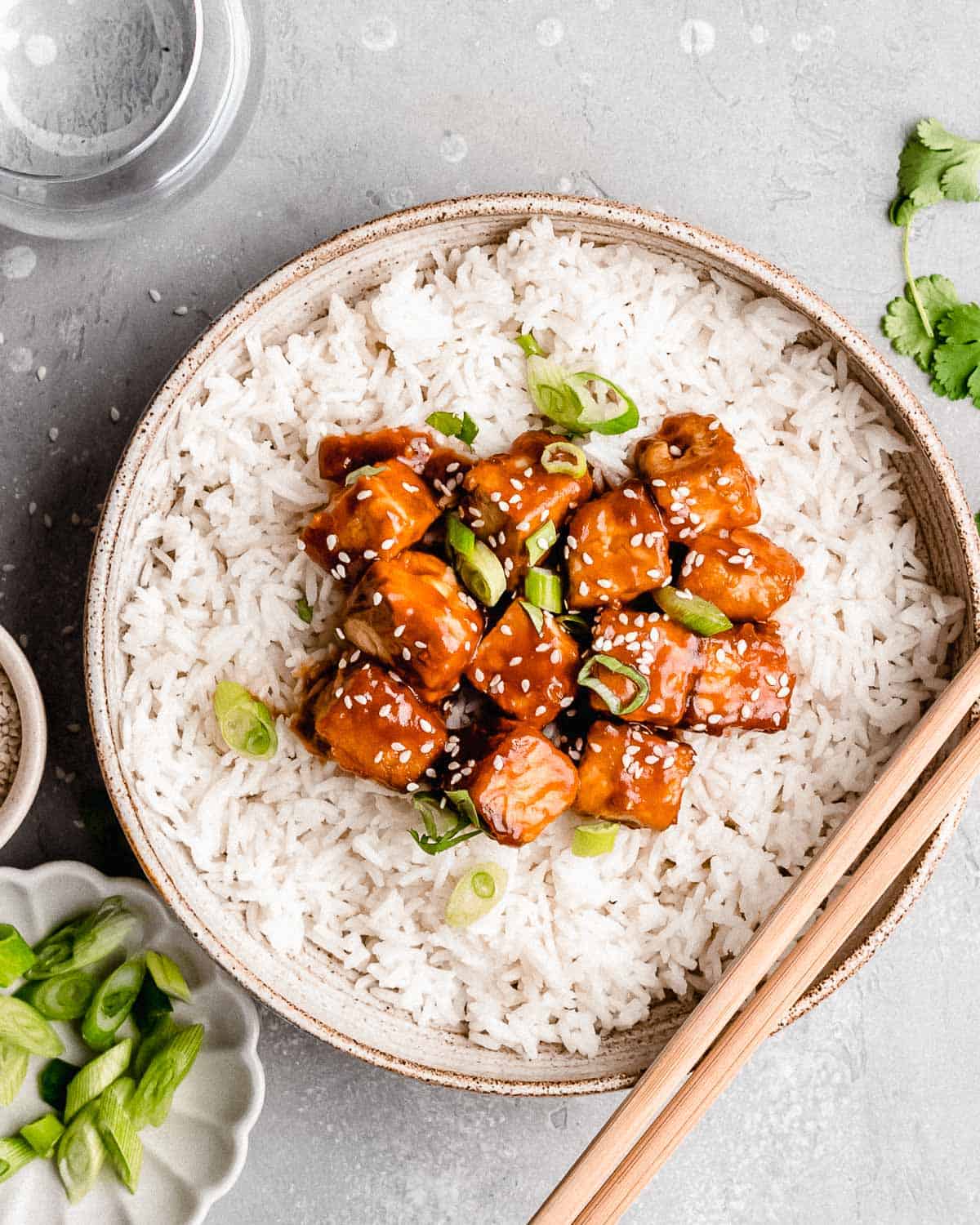 sticky tofu topped with sesame seeds on a bowl of white rice.