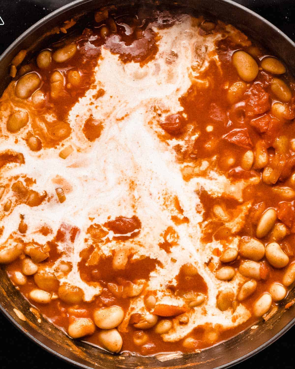butter beans in tomato sauce with coconut milk added in a pan.