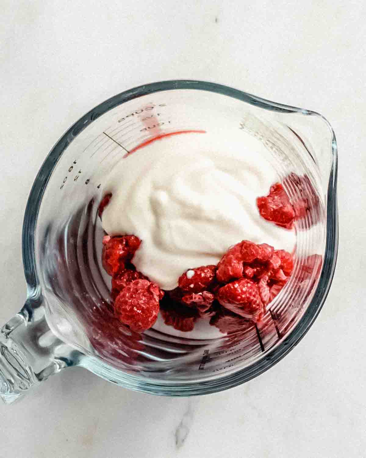 defrosted raspberries and yogurt in a glass measuring cup.