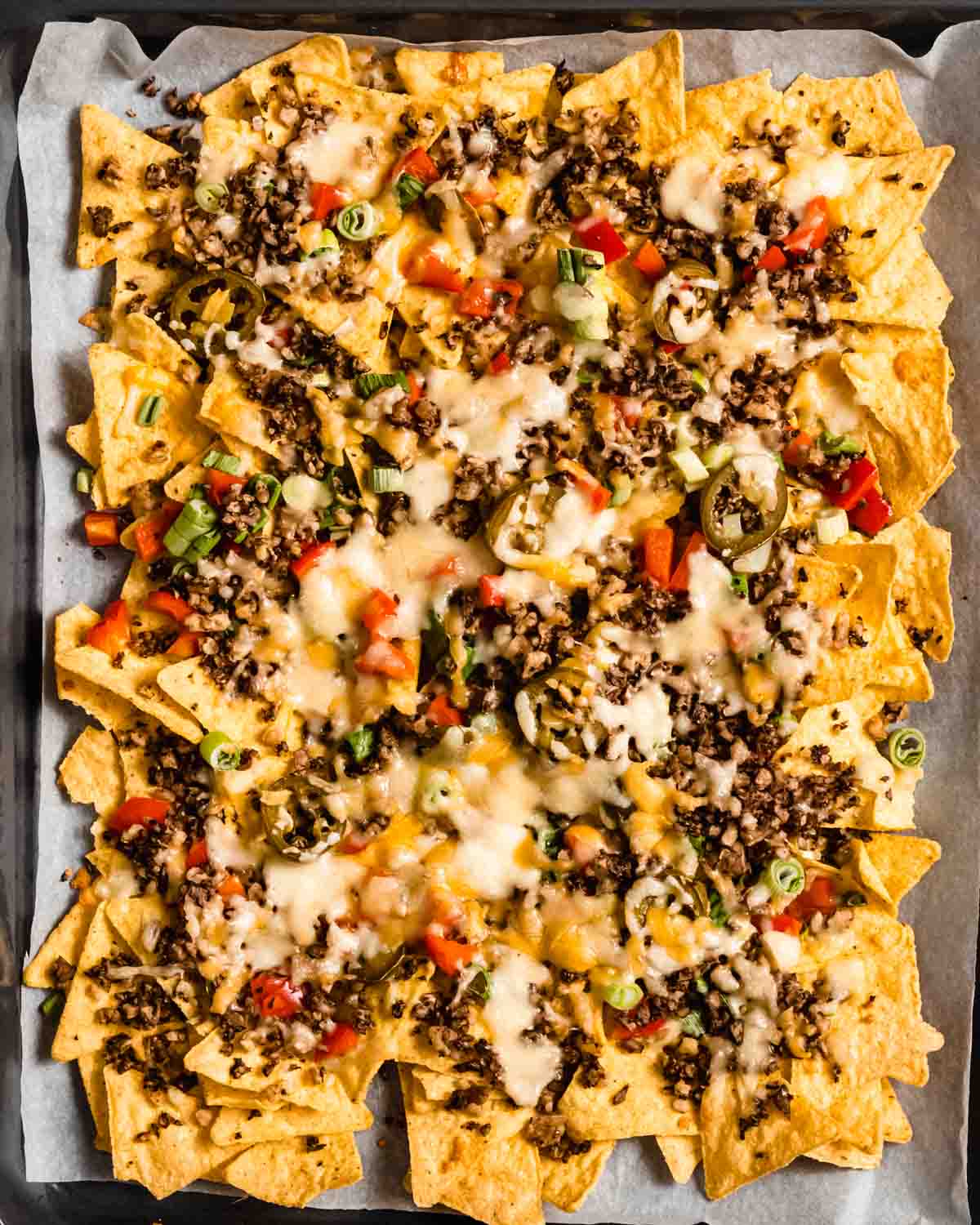 loaded veggie nachos on a sheet pan lined with parchment paper.